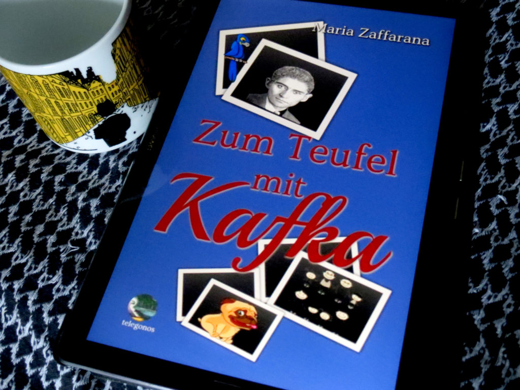 E-Book "Zum Teufel mit Kafka" von Maria Zaffarana, daneben eine Tasse mit der silhouette Franz Kafkas vor den gelben Fassaden Prags