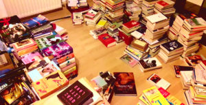Mehrere hundert Bücher, hauptsächlich Belletristik, in chaotischen Stapeln über den Boden verteilt.